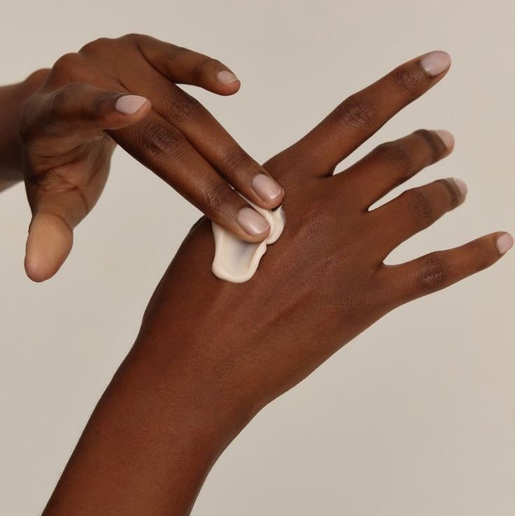 Two hands applying cream to a palm against a beige background